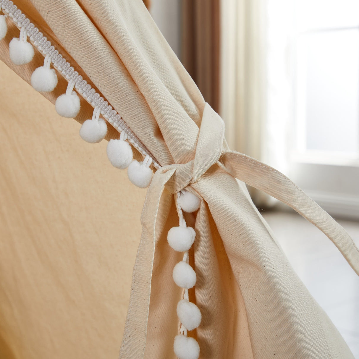 Beige curtain with white pom-pom trim in front of a window