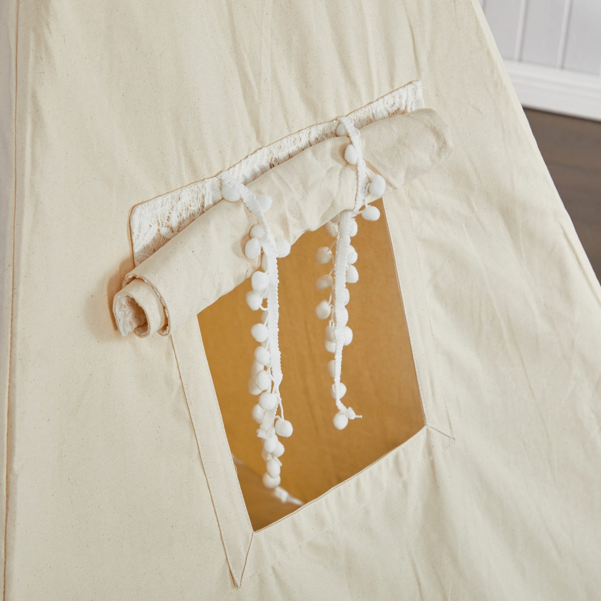 Beige fabric tent with a window and decorative tassels on a plain background