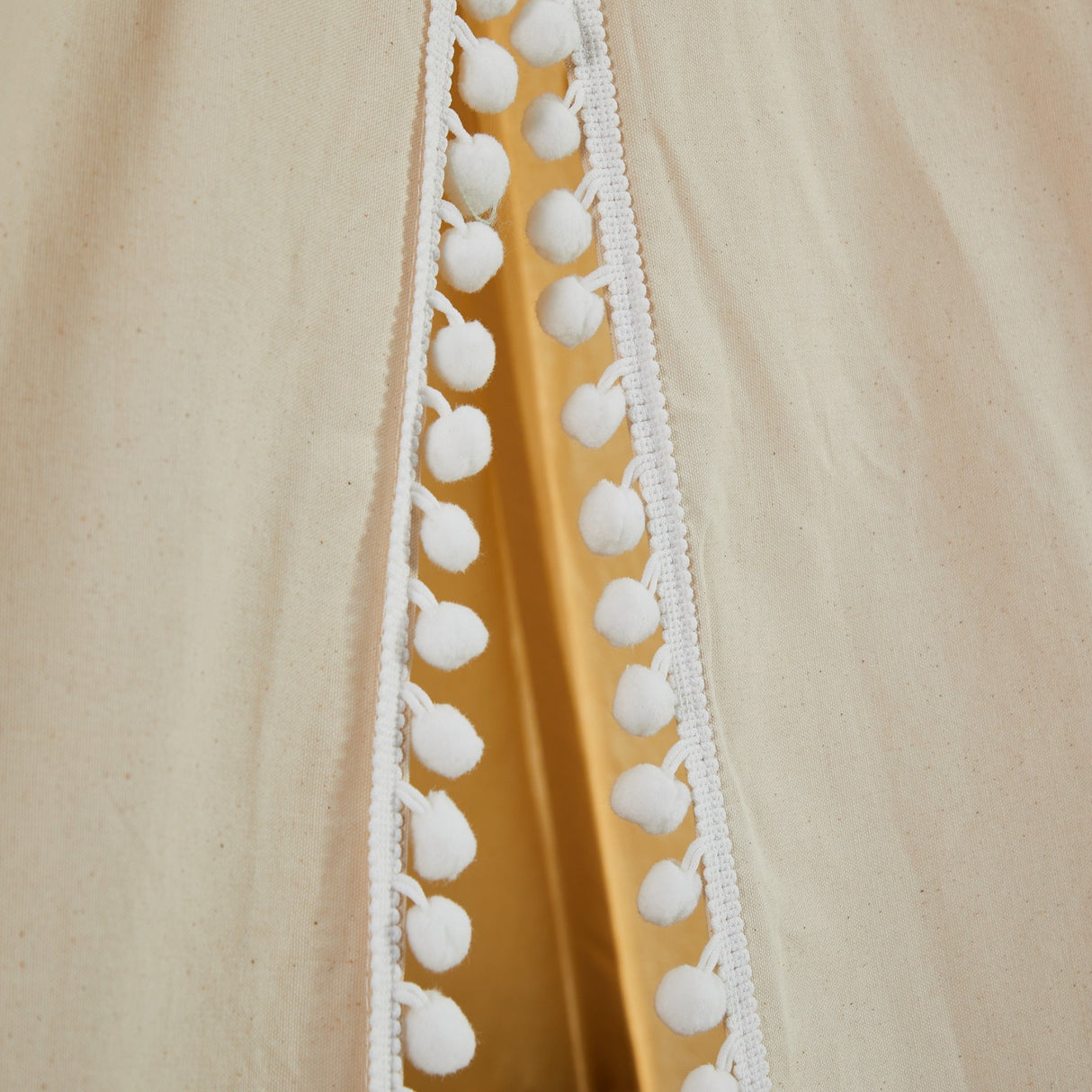 Close-up of a garment with white pom-pom trim on a beige background
