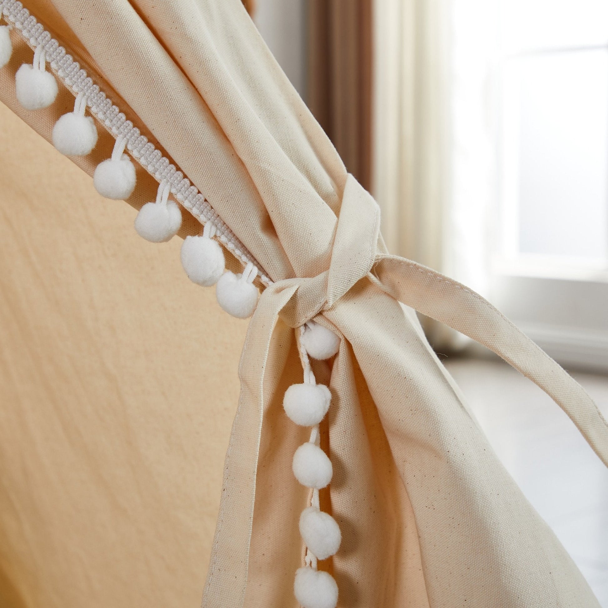 Beige curtain with white pom-pom trim in front of a window