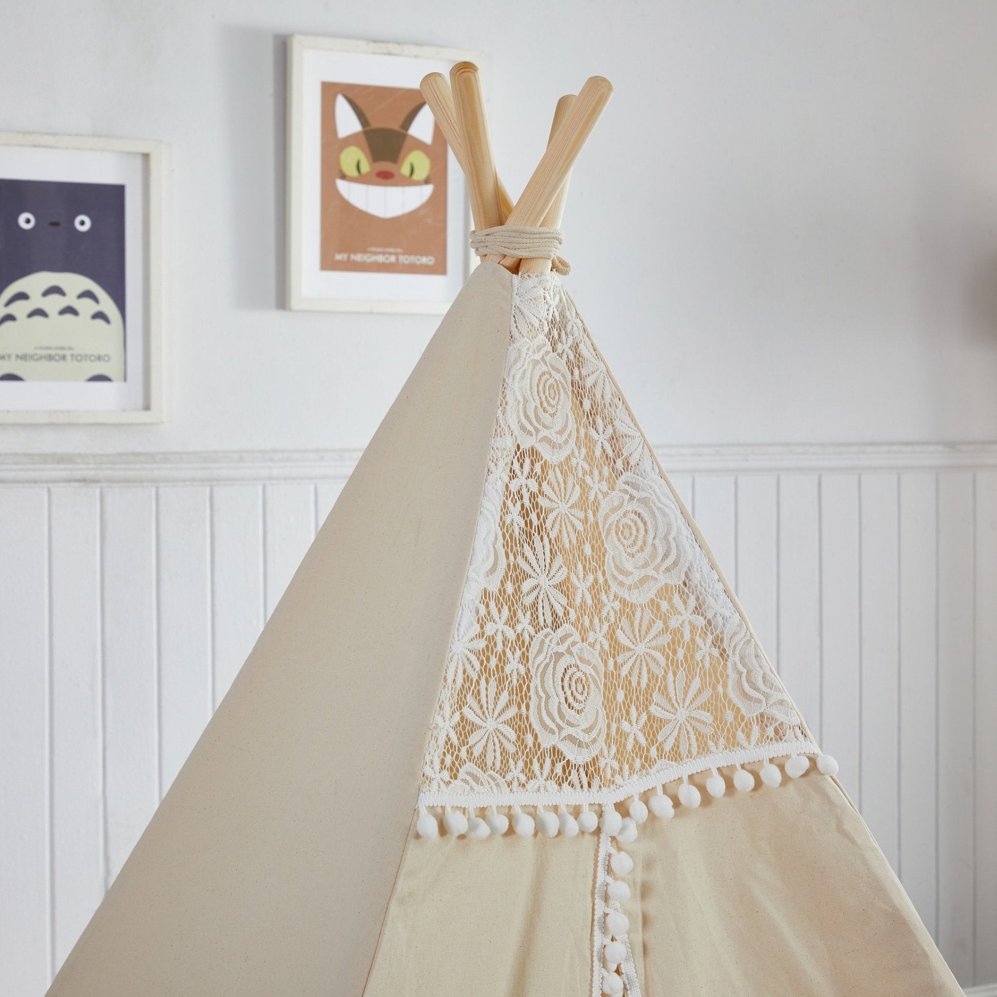 Beige teepee with lace detailing against a white wall with framed pictures.